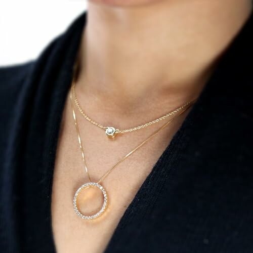 Close-up of person wearing layered gold necklaces with pendant.