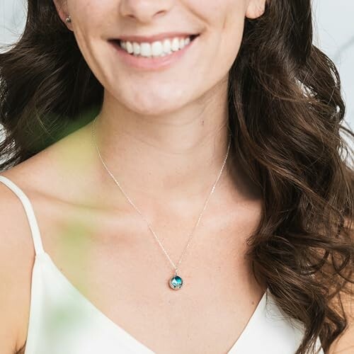 Woman smiling, wearing a necklace with a blue pendant